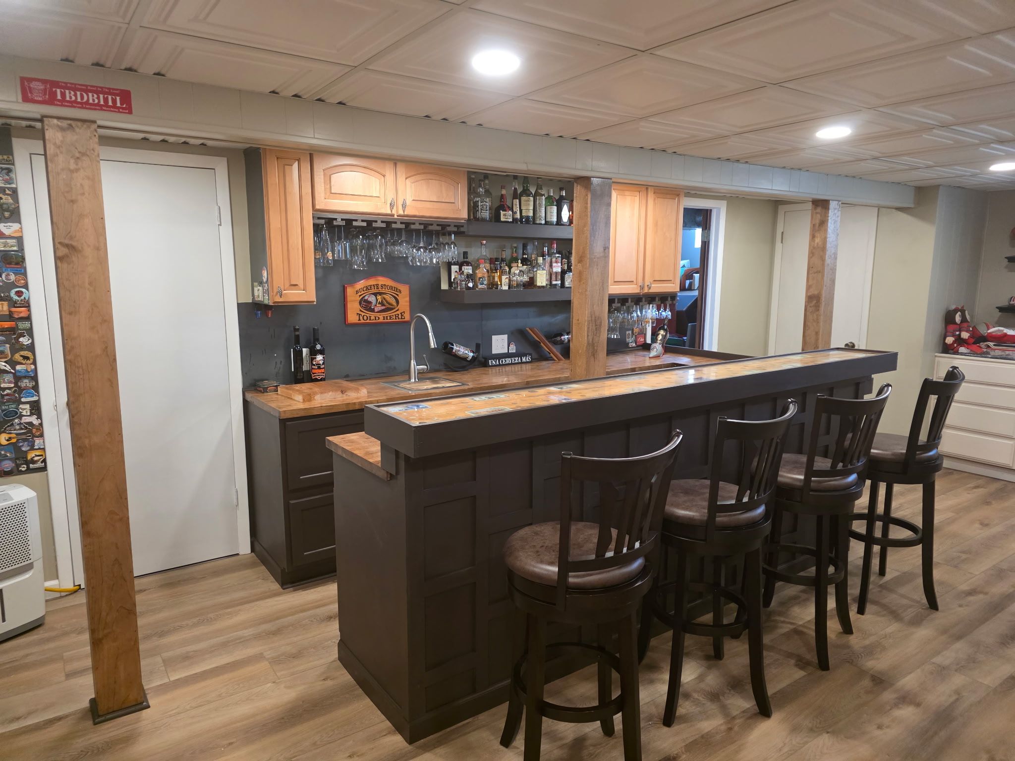 Finished basement bar with dark paneled front, wood counter, bar stools and upper cabinets.