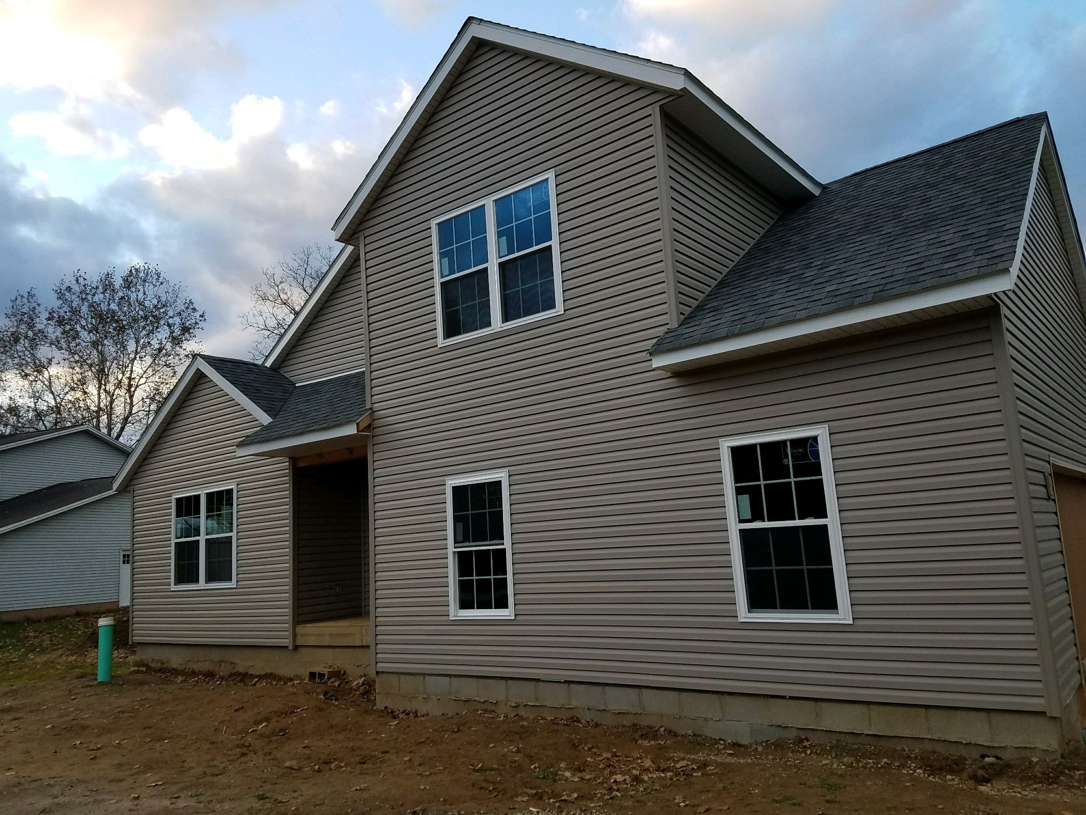 New two-story house with gray siding, seen from the front corner with the roofline and garage.