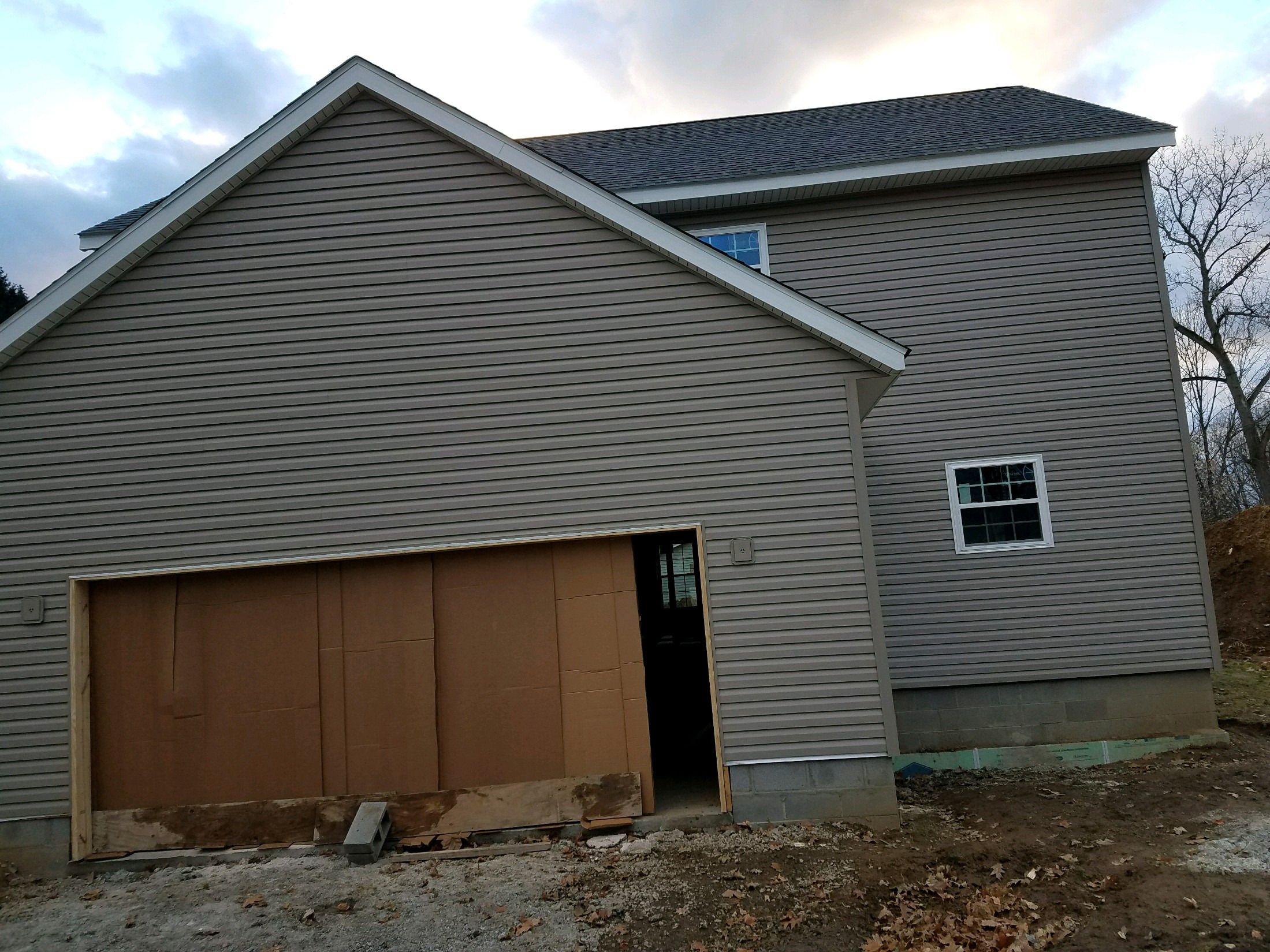 Garage side of the new home with siding and a temporarily boarded garage opening.