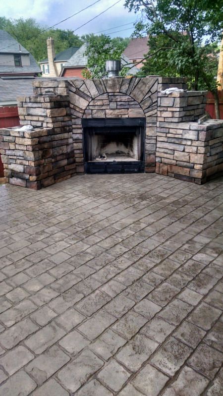 Stone outdoor fireplace with arched opening and built-in side walls on a paver patio.